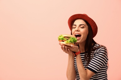 Young woman eating tasty burger on color background. Space for text