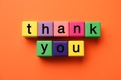 Photo of Colorful cubes with phrase Thank You on orange background, top view