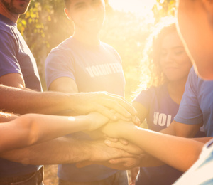 Image of Group of volunteers joining hands together outdoors on sunny day