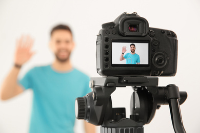 Photo of Young blogger shooting video with camera against white background, focus on screen