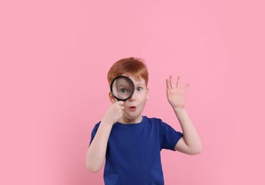 Surprised boy looking through magnifier glass on pink background