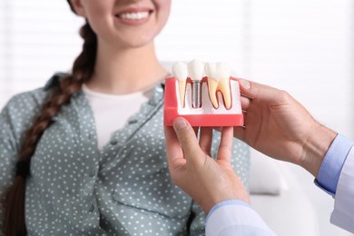 Photo of Doctor with educational model of dental implant consulting patient in clinic, closeup