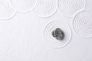 Photo of Zen garden stones on white sand with pattern, top view. Space for text