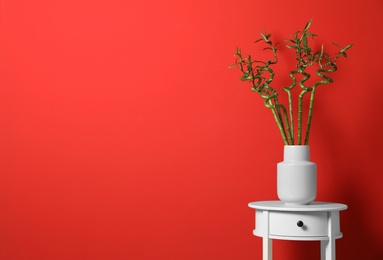 Vase with bamboo stems on white table against red background, space for text