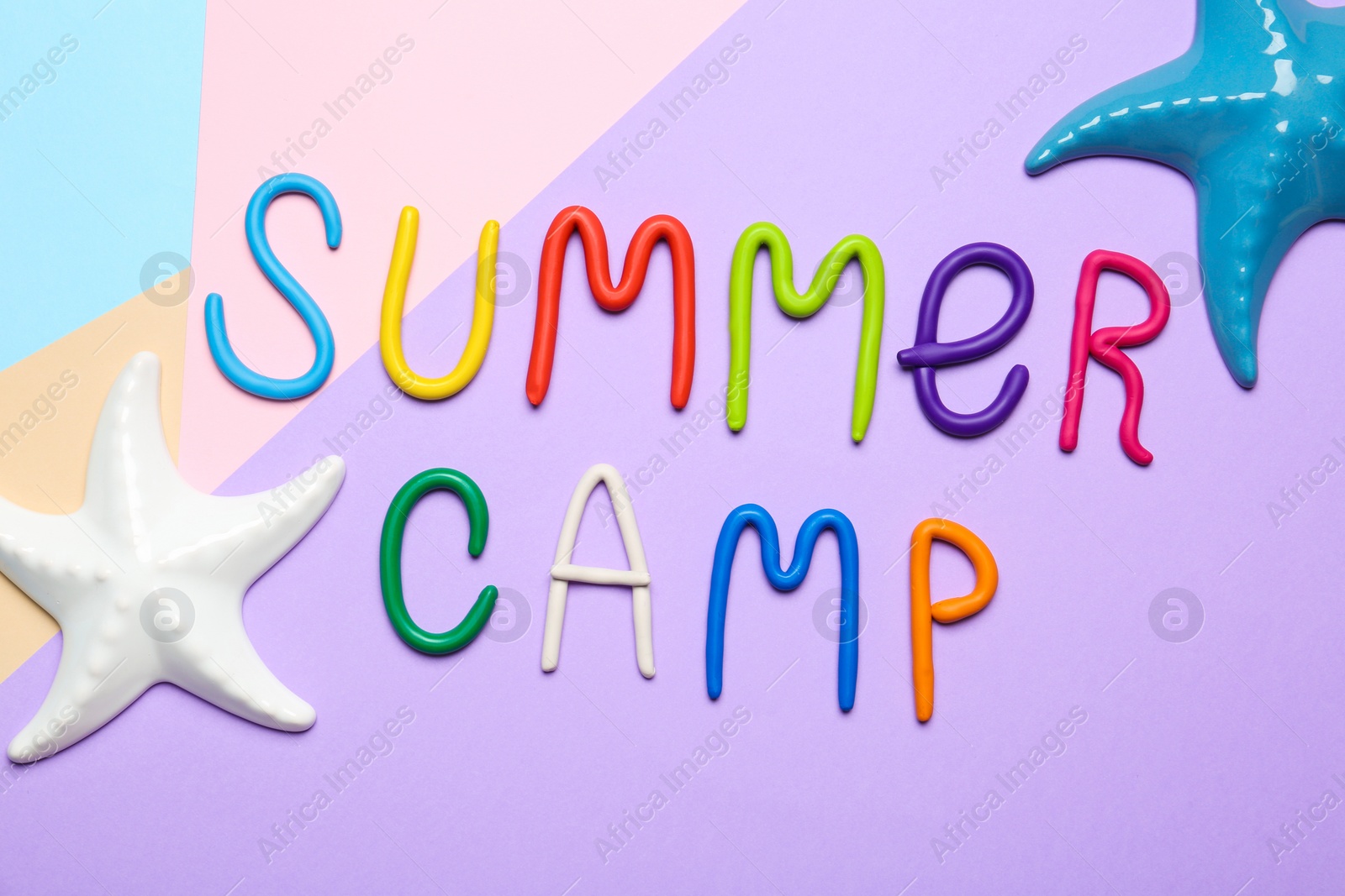Photo of Text SUMMER CAMP made of modelling clay and decorative starfishes on color background, flat lay