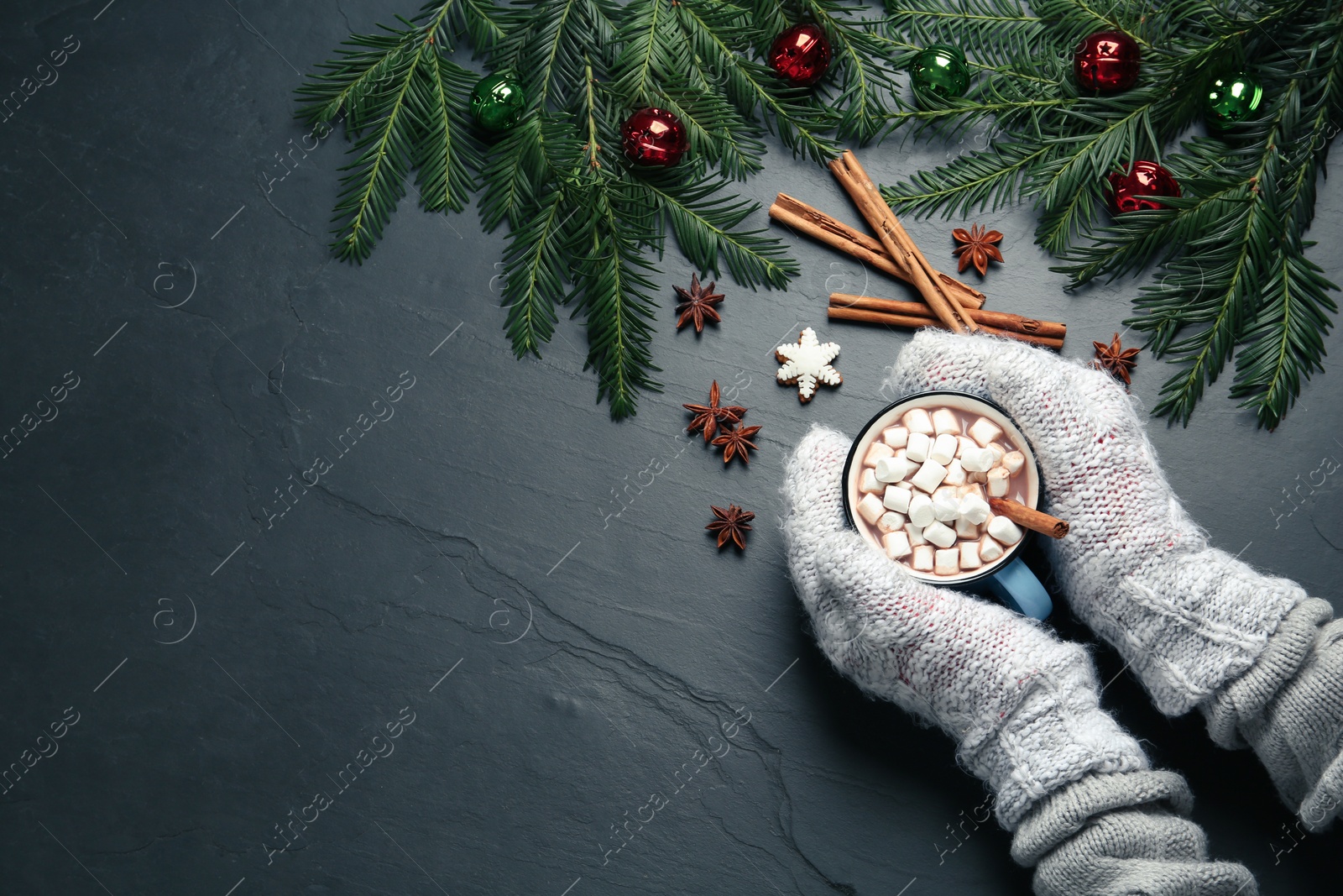 Photo of Woman in knitted mittens holding cup of delicious hot chocolate with marshmallows at black table, top view. Space for text