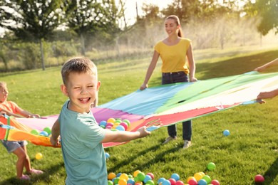 Photo of Group of children and teacher playing with rainbow playground parachute on green grass. Summer camp activity