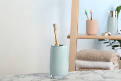 Photo of Holder with bamboo toothbrush on table against blurred background