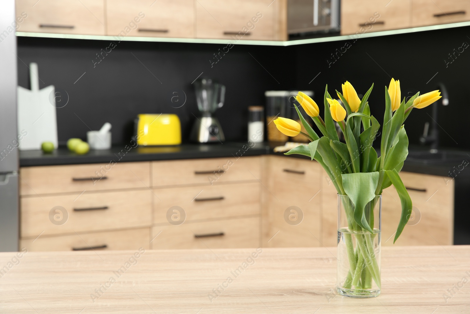 Photo of Glass vase with tulips on table in kitchen