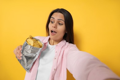 Photo of Woman taking selfie with potato chips on orange background