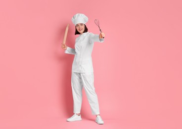 Photo of Happy confectioner with rolling pin and whisk on pink background