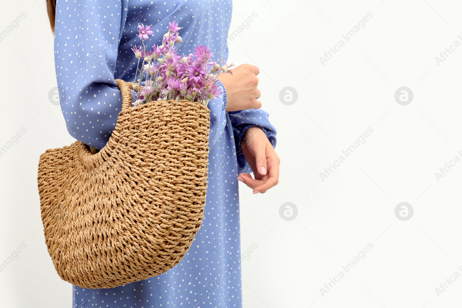 Photo of Woman holding beach bag with beautiful bouquet of wildflowers on white background, closeup