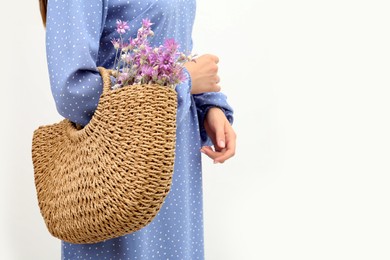 Woman holding beach bag with beautiful bouquet of wildflowers on white background, closeup