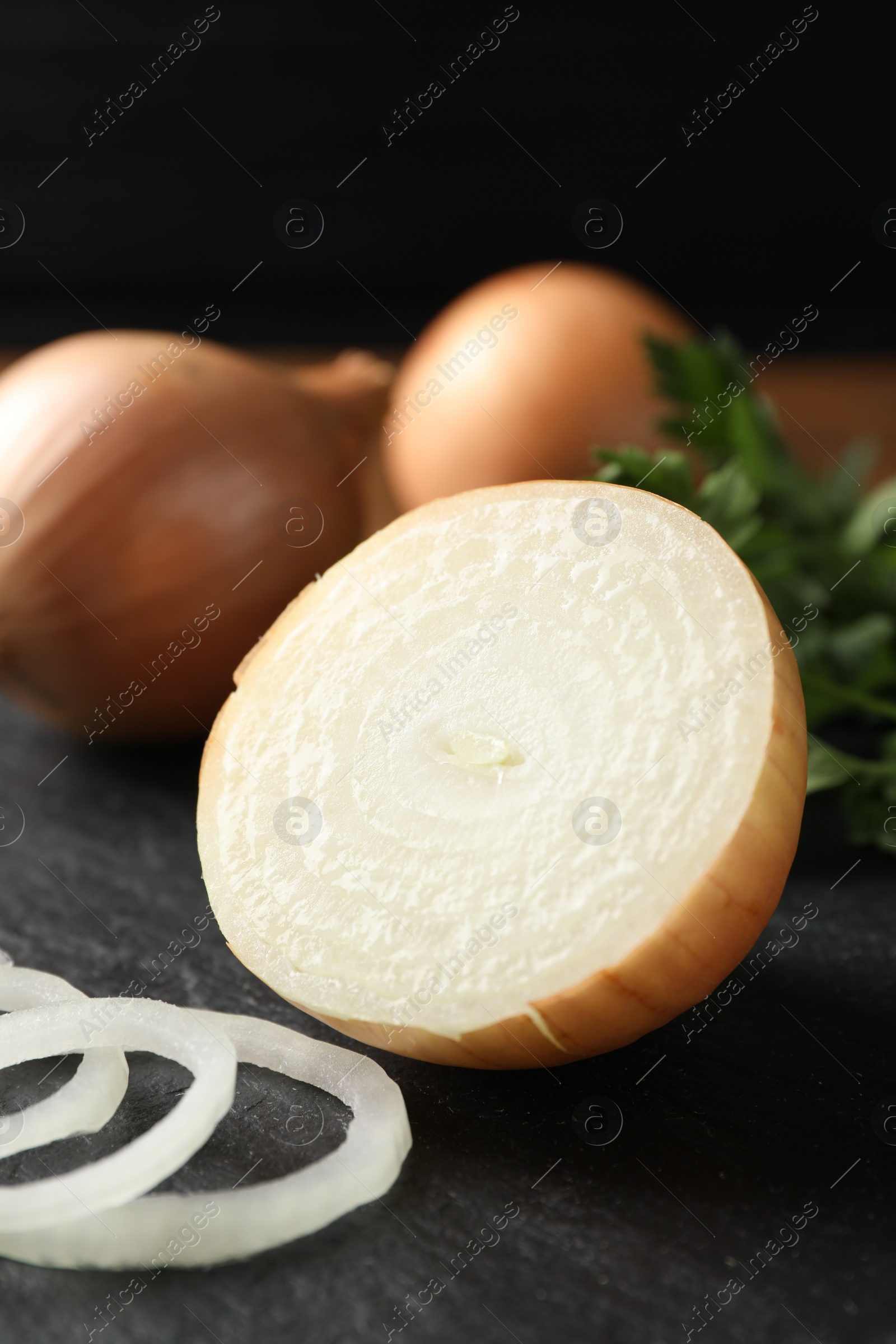 Photo of Whole and cut onions on black textured table, closeup