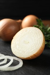 Photo of Whole and cut onions on black textured table, closeup