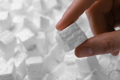 Woman holding small styrofoam cube on blurred background, closeup. Space for text