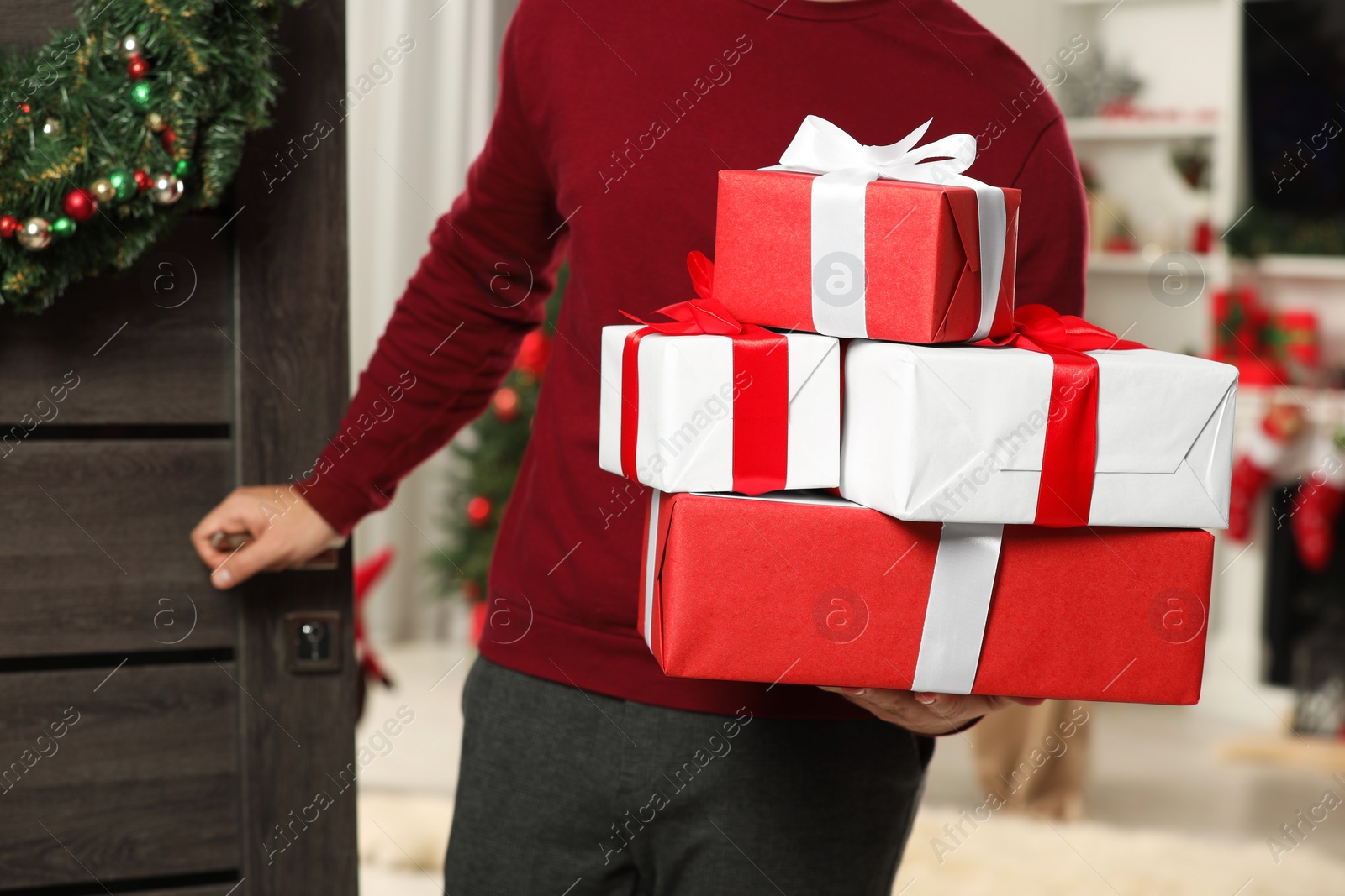 Photo of Young man in Santa hat with Christmas gift boxes indoors, closeup. Sending present by mail