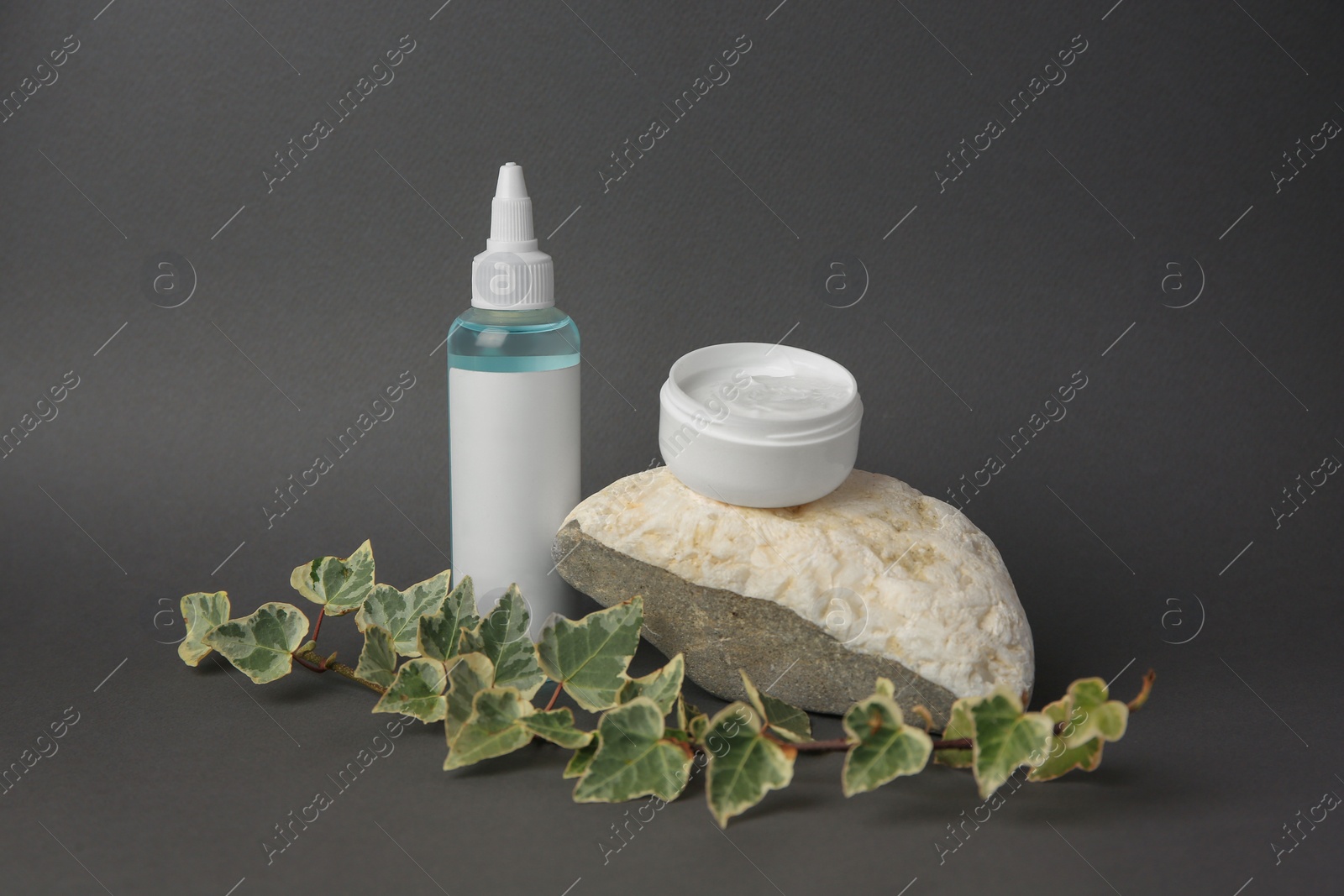 Photo of Cosmetic products, stone and ivy leaves on dark grey background