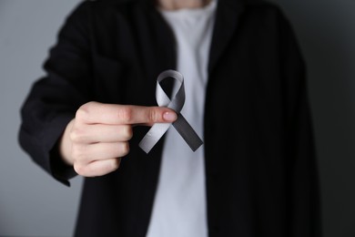 Photo of Woman holding grey awareness ribbon on color background, closeup