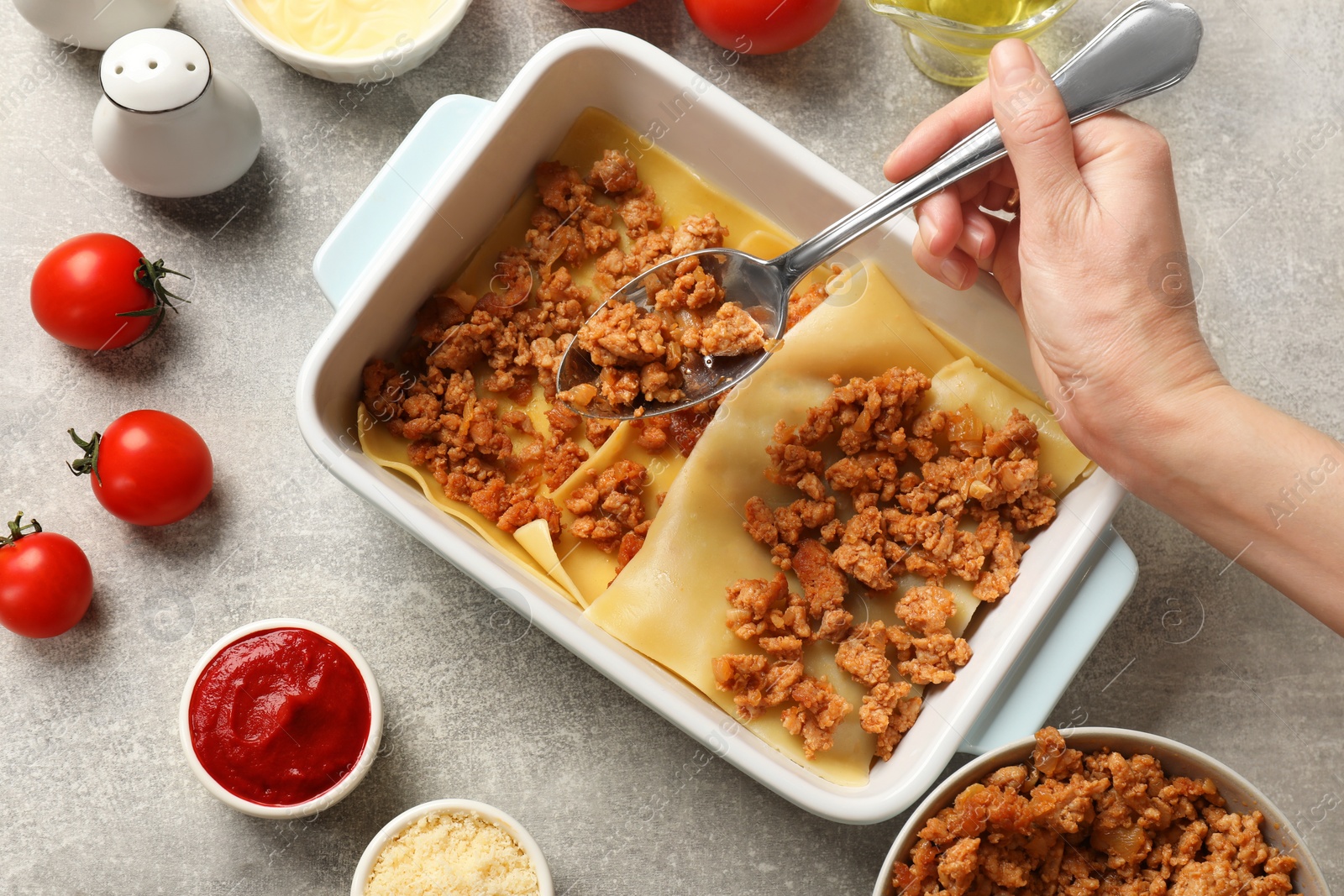 Photo of Woman making lasagna at light grey textured table, top view