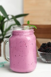 Photo of Delicious blackberry smoothie in mason jar and berries on white table indoors