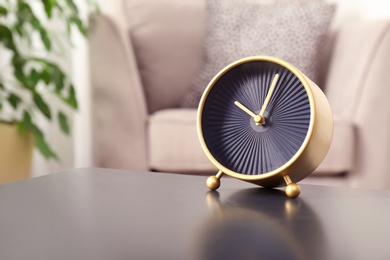 Stylish analog clock on table in living room, space for text. Time of day