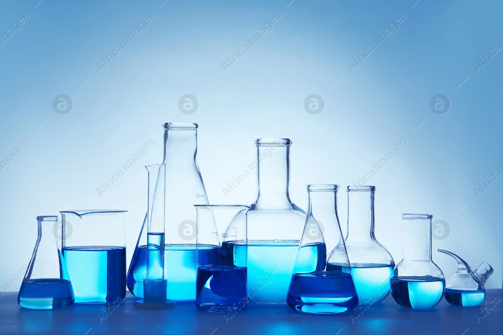 Photo of Laboratory glassware for chemical analysis with blue liquid on table against white background