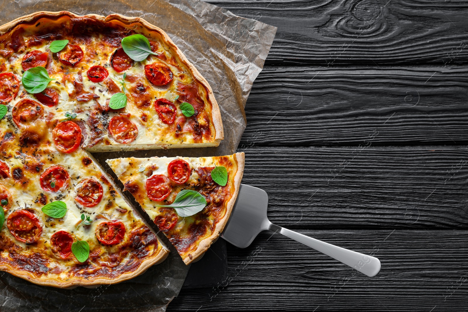 Photo of Cut delicious homemade quiche with prosciutto and server on black wooden table, top view. Space for text