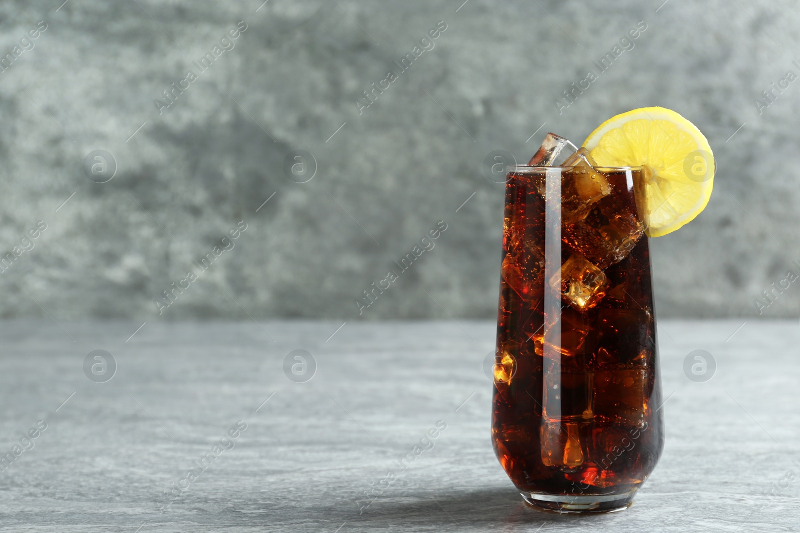 Photo of Glass of refreshing soda water with ice cubes and lemon slice on grey table, space for text