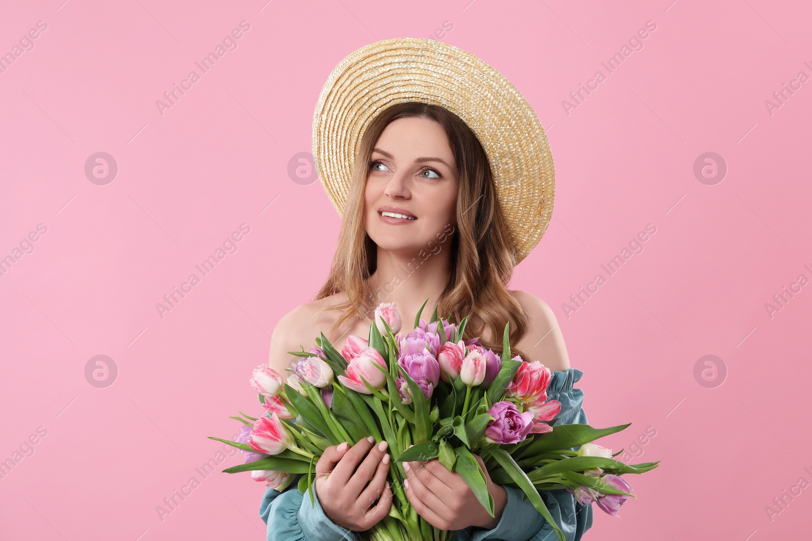 Photo of Happy young woman in straw hat holding bouquet of beautiful tulips on pink background