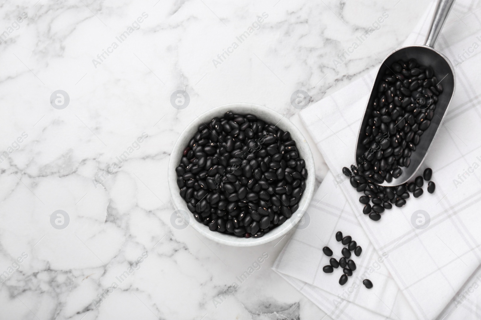 Photo of Bowl and scoop of raw black beans on white marble table, flat lay. Space for text