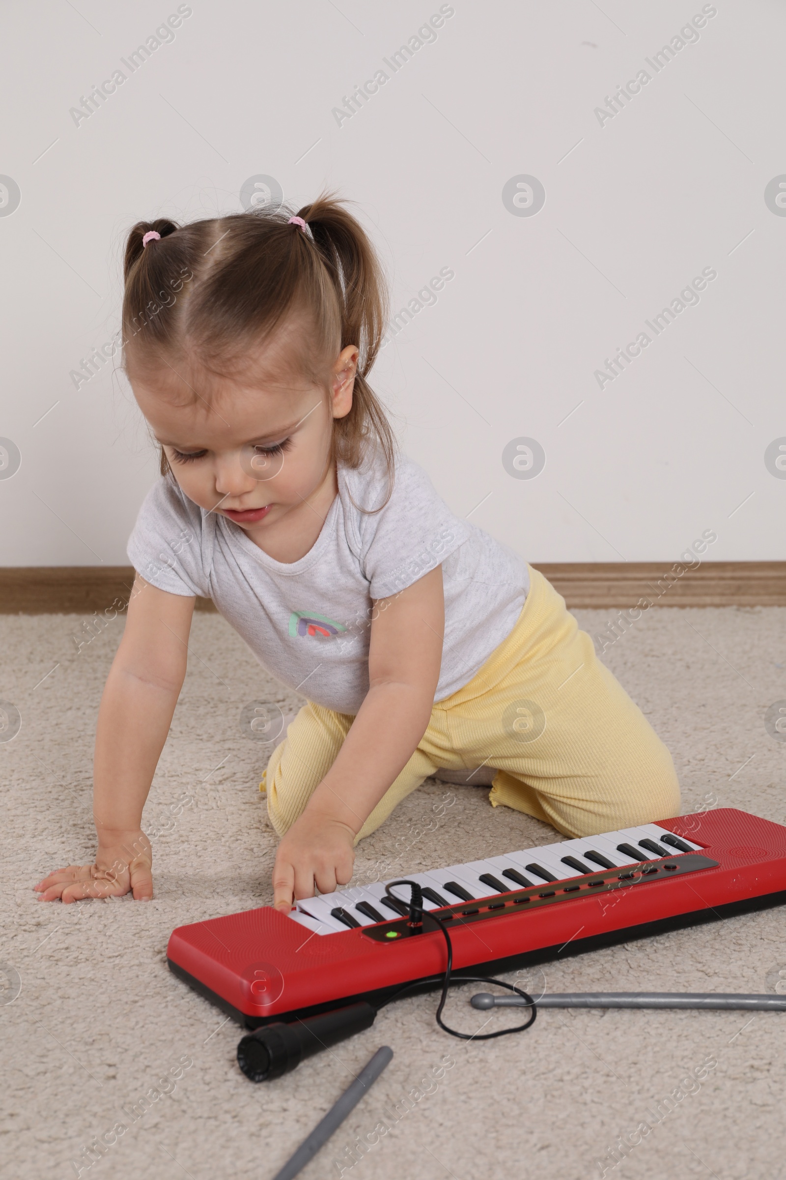 Photo of Cute little girl playing with toy piano at home