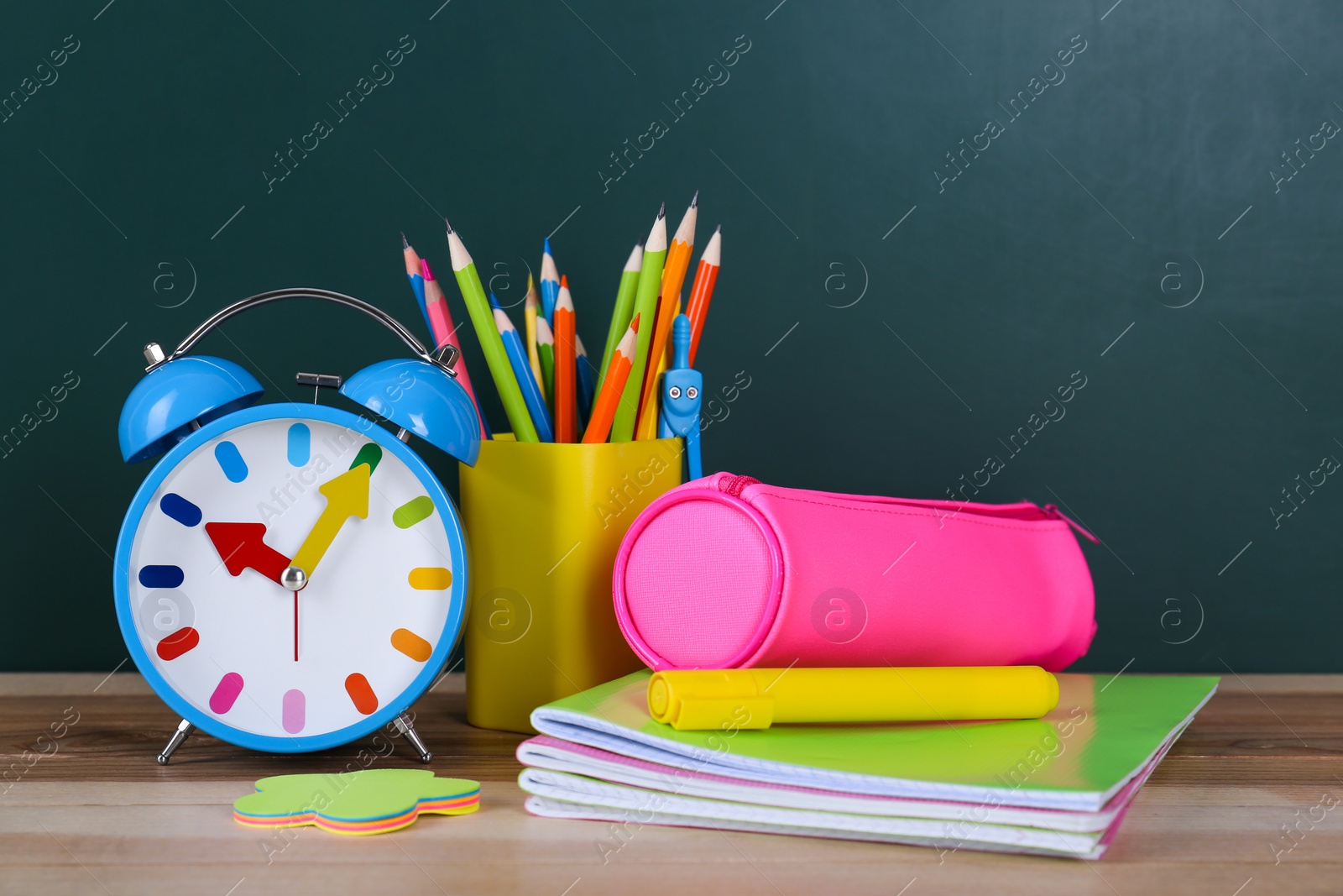 Photo of Composition with stationery and alarm clock on table near chalkboard. Doing homework