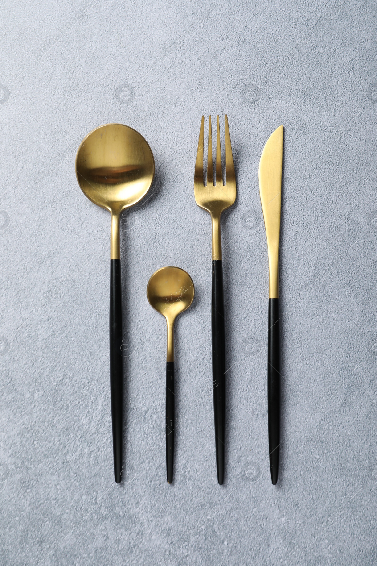 Photo of Stylish golden cutlery on grey table, flat lay