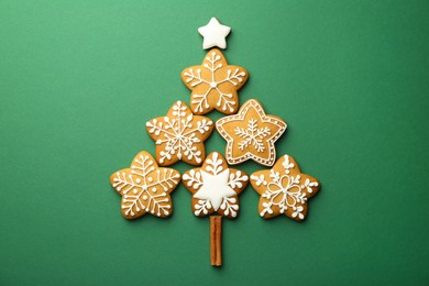 Photo of Christmas tree made of tasty cookies with icing and cinnamon stick on green background, flat lay
