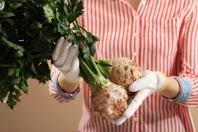 Photo of Woman holding raw celery roots on beige background, closeup