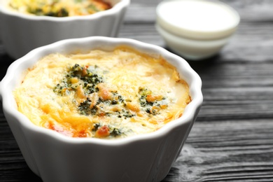 Photo of Tasty broccoli casserole in ramekin on black wooden table, closeup