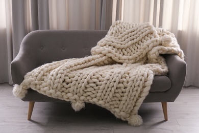 Photo of Soft knitted blanket on couch in living room. Interior element