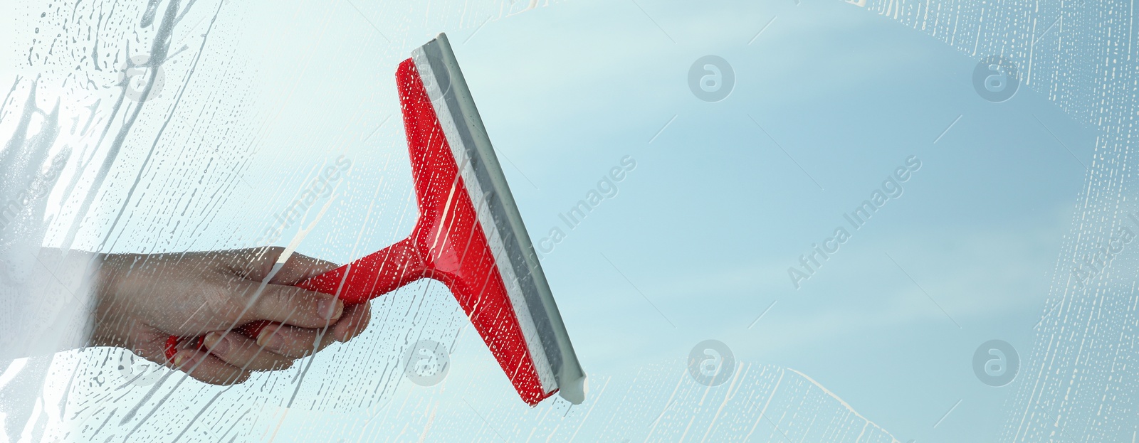 Image of Woman cleaning window with squeegee on spring day, closeup view. Banner design