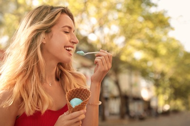 Happy young woman with delicious ice cream in waffle cone outdoors. Space for text