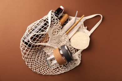 Photo of Fishnet bag with different items on brown background, top view. Conscious consumption