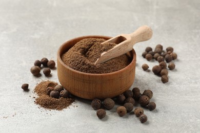 Photo of Ground allspice pepper in bowl, grains and scoop on grey table