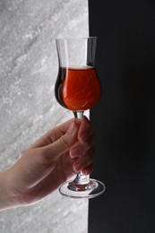 Photo of Woman holding glass of delicious liqueur on color background, closeup