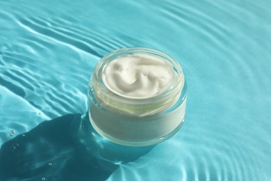 Photo of Jar with moisturizing cream in water on light blue background