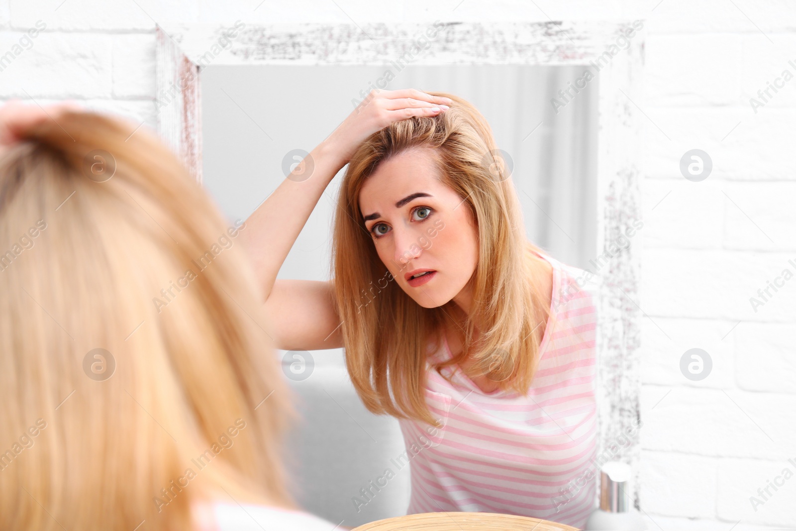 Photo of Young woman with hair loss problem near mirror indoors
