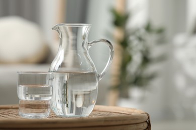 Photo of Jug and glass with clear water on wicker surface against blurred background, closeup. Space for text