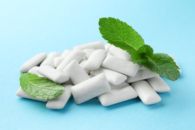 Pile of tasty white chewing gums and mint leaves on light blue background, closeup