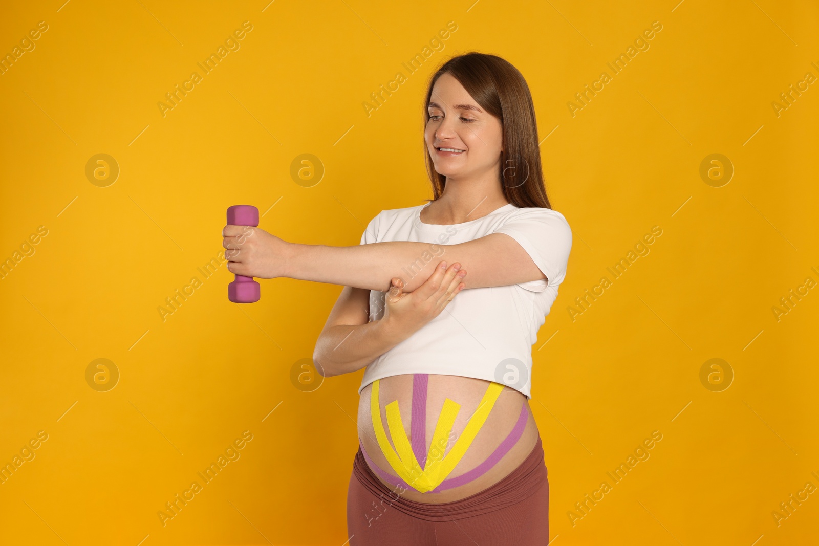 Photo of Pregnant woman with kinesio tapes on her belly doing exercises against orange background