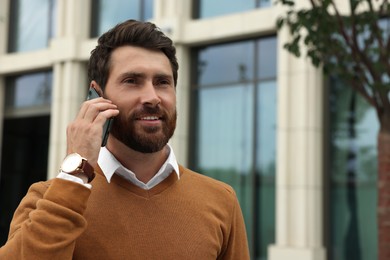 Handsome man talking on phone while walking outdoors, space for text