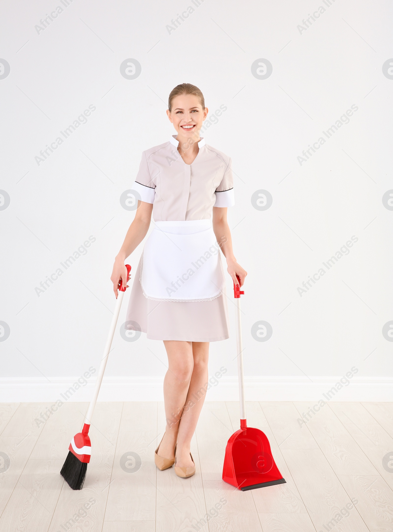 Photo of Young chambermaid with broom and dustpan  indoors